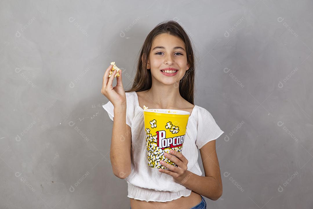 Linda adolescente caucasiana comendo pipoca em fundo neutro para texto. Conceito de entretenimento de férias. menina comendo pipoca