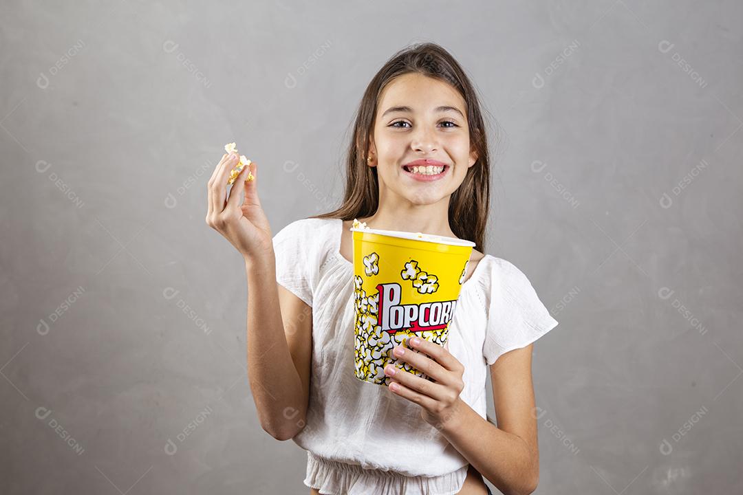 Linda adolescente caucasiana comendo pipoca em fundo neutro para texto. Conceito de entretenimento de férias. menina comendo pipoca