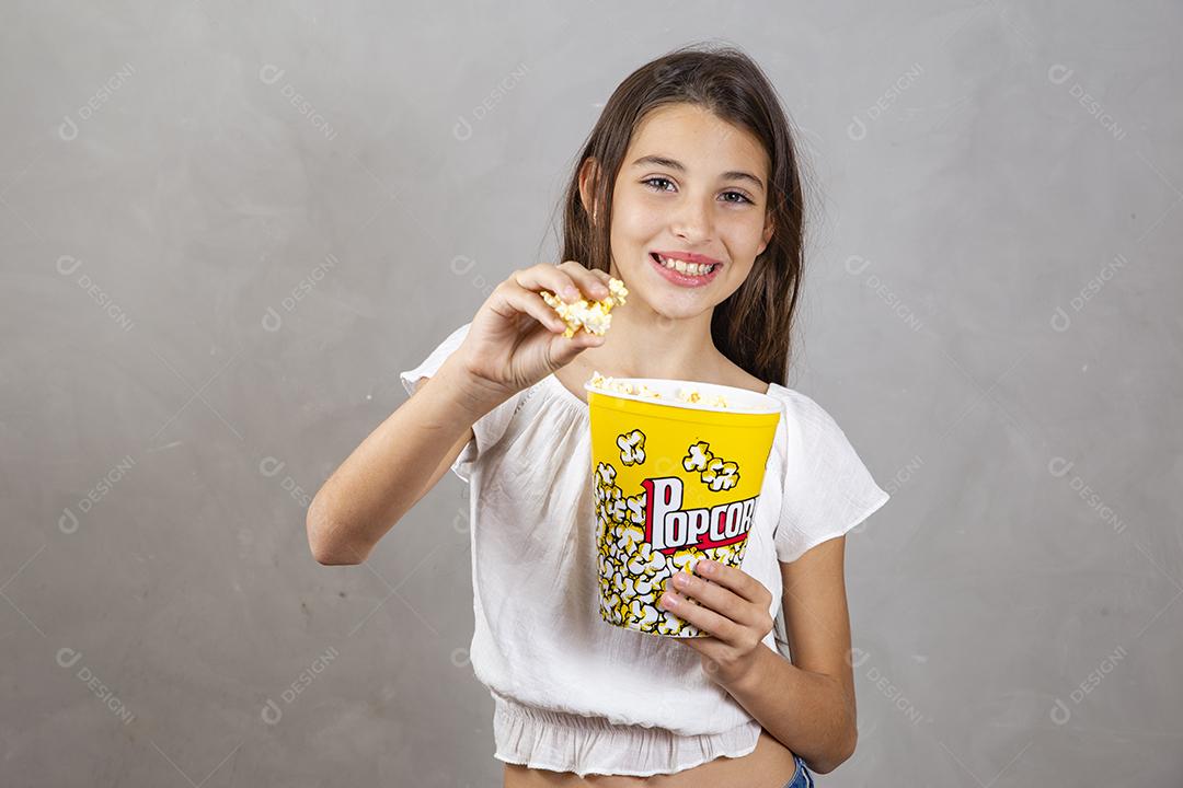 Linda adolescente caucasiana comendo pipoca em fundo neutro para texto. Conceito de entretenimento de férias. menina comendo pipoca