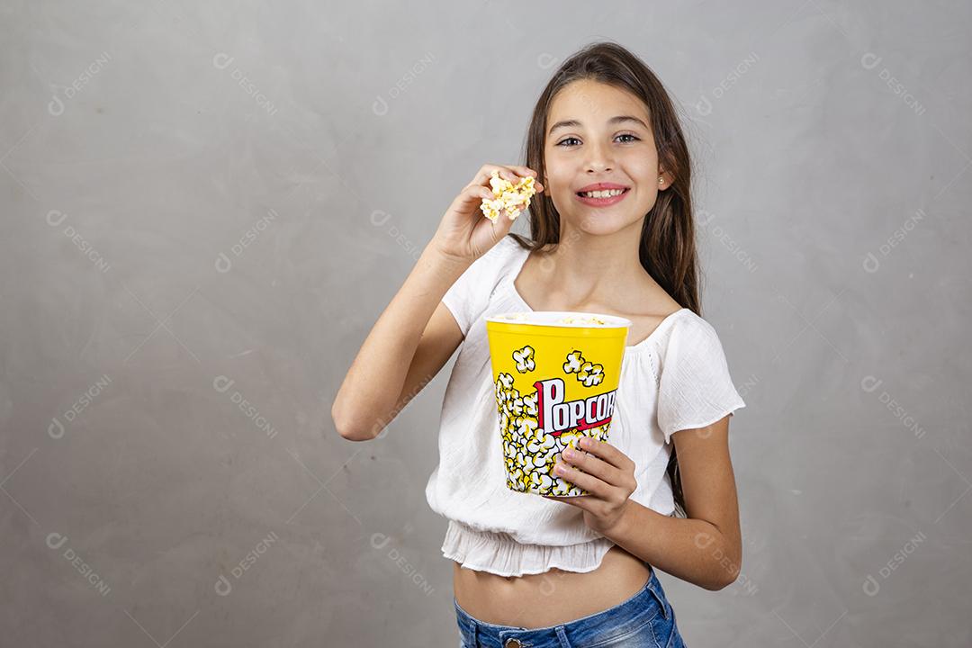 Linda adolescente caucasiana comendo pipoca em fundo neutro para texto. Conceito de entretenimento de férias. menina comendo pipoca