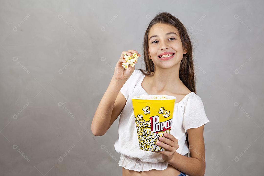 Linda adolescente caucasiana comendo pipoca em fundo neutro para texto. Conceito de entretenimento de férias. menina comendo pipoca