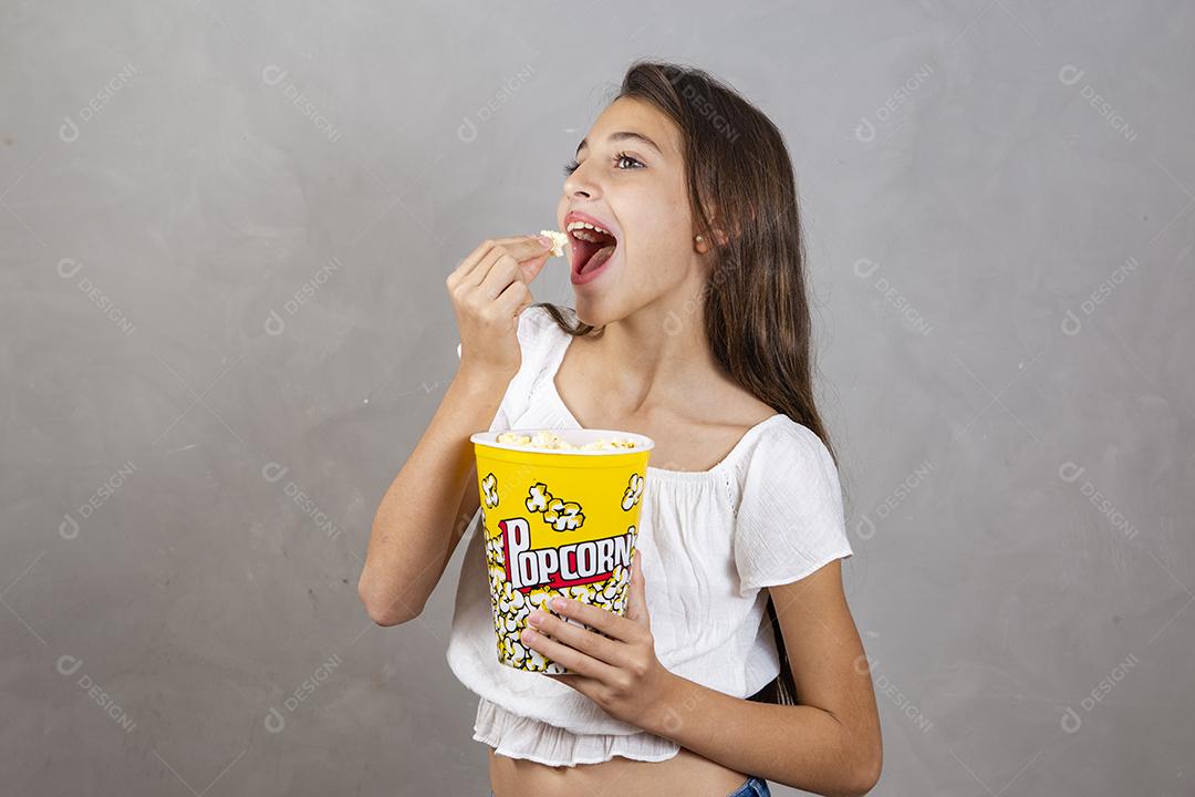 Linda adolescente caucasiana comendo pipoca em fundo neutro para texto. Conceito de entretenimento de férias. menina comendo pipoca