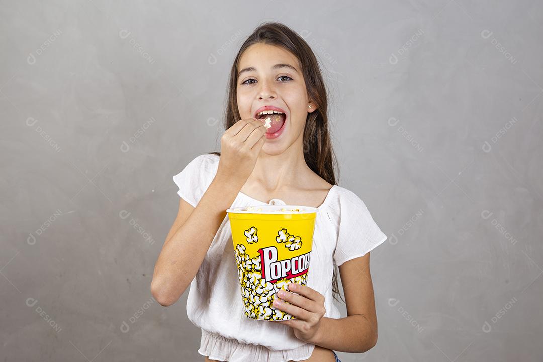 Linda adolescente caucasiana comendo pipoca em fundo neutro para texto. Conceito de entretenimento de férias. menina comendo pipoca