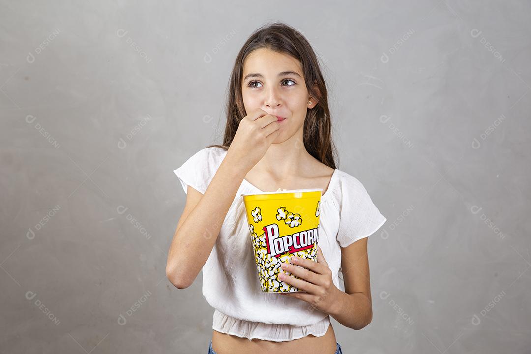 Linda adolescente caucasiana comendo pipoca em fundo neutro para texto. Conceito de entretenimento de férias. menina comendo pipoca