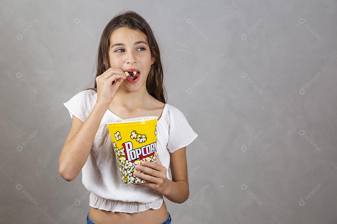 Linda adolescente caucasiana comendo pipoca em fundo neutro para texto. Conceito de entretenimento de férias. menina comendo pipoca