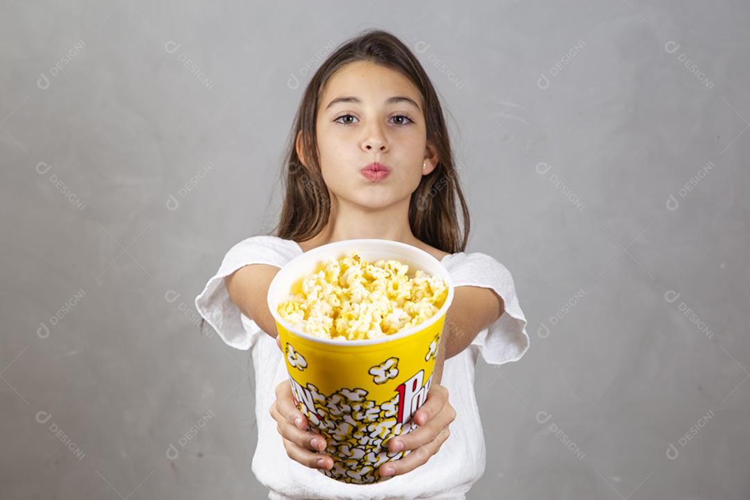 Linda adolescente caucasiana comendo pipoca em fundo neutro para texto. Conceito de entretenimento de férias. menina comendo pipoca