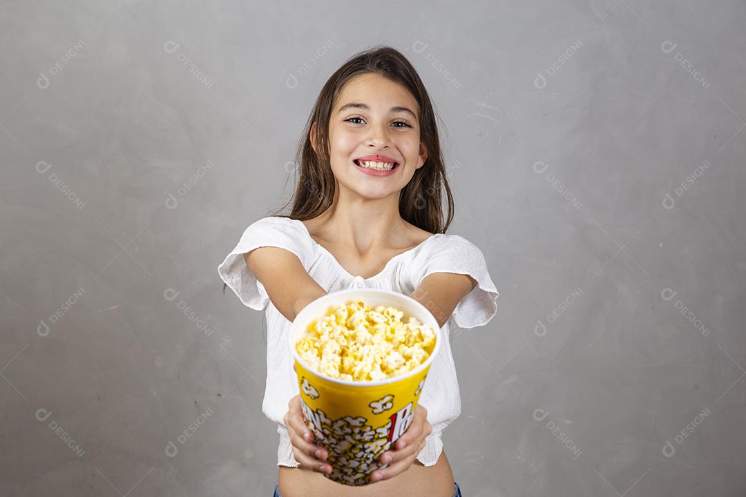 Linda adolescente caucasiana comendo pipoca em fundo neutro para texto. Conceito de entretenimento de férias. menina comendo pipoca