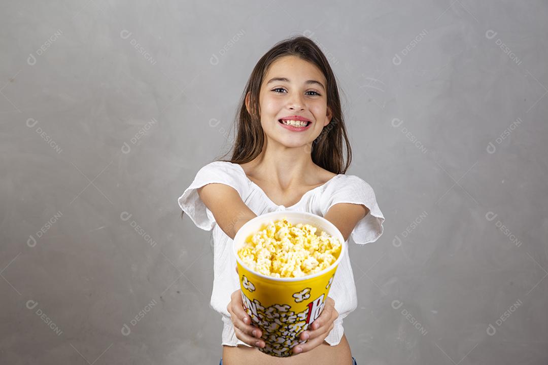 Linda adolescente caucasiana comendo pipoca em fundo neutro para texto. Conceito de entretenimento de férias. menina comendo pipoca