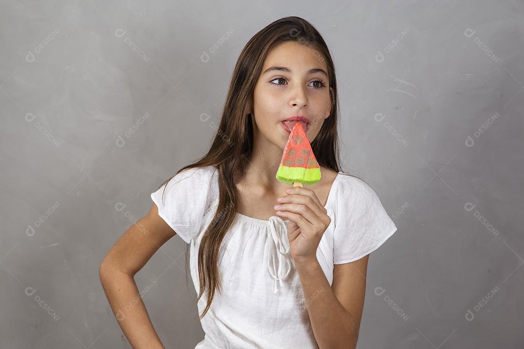 Adorável menina com delicioso picolé de sorvete no fundo cinza