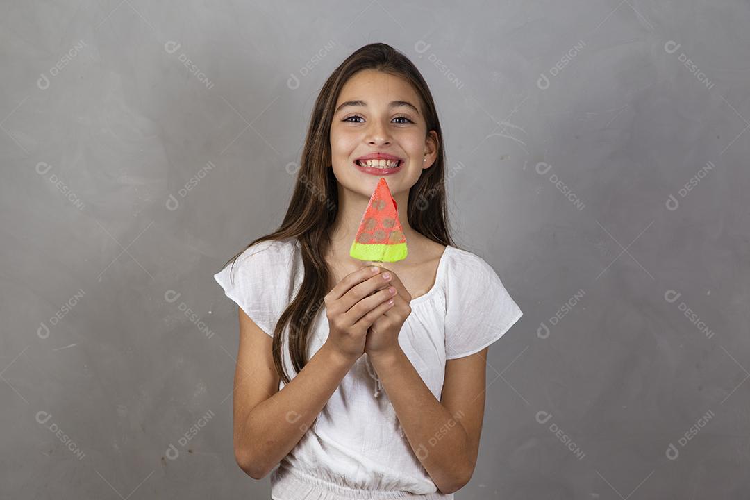 Adorável menina com delicioso picolé de sorvete no fundo cinza