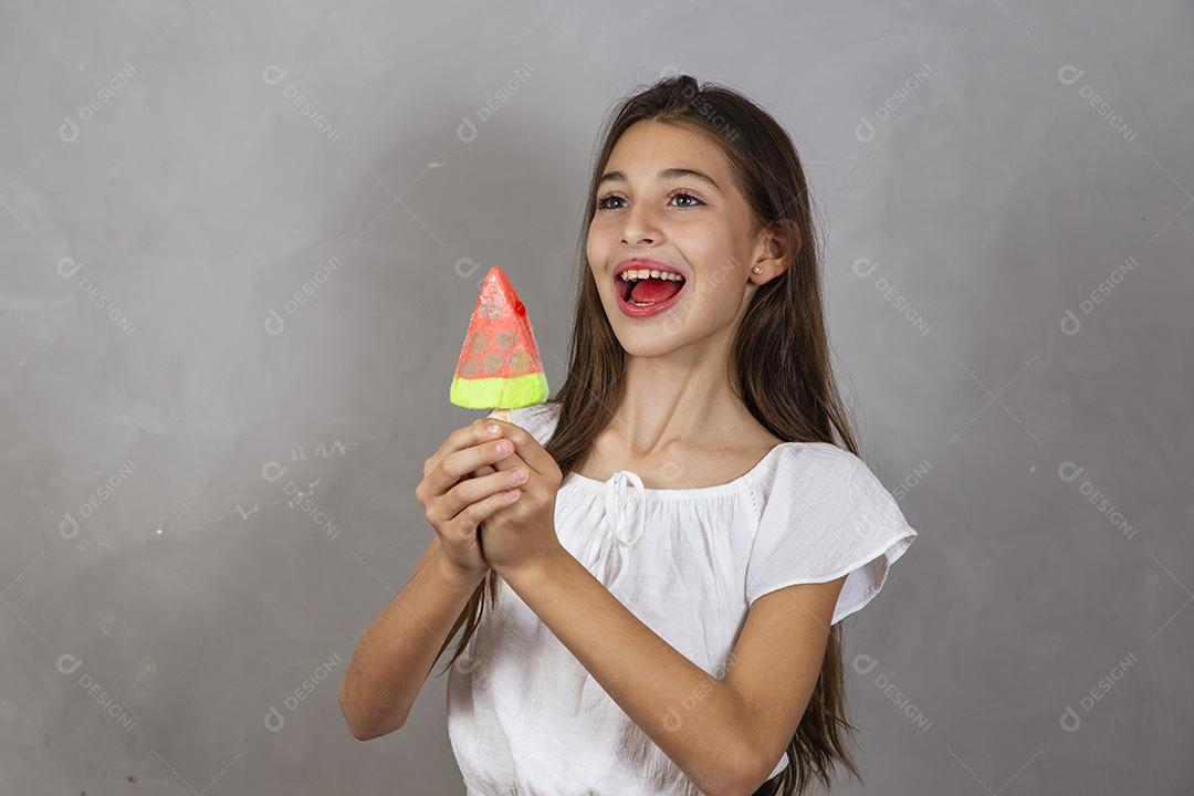 Adorável menina com delicioso picolé de sorvete no fundo cinza