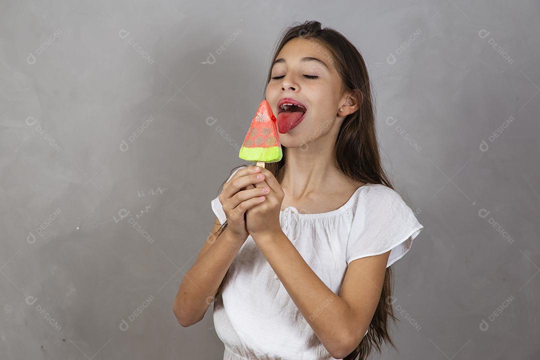 Adorável menina com delicioso picolé de sorvete no fundo cinza