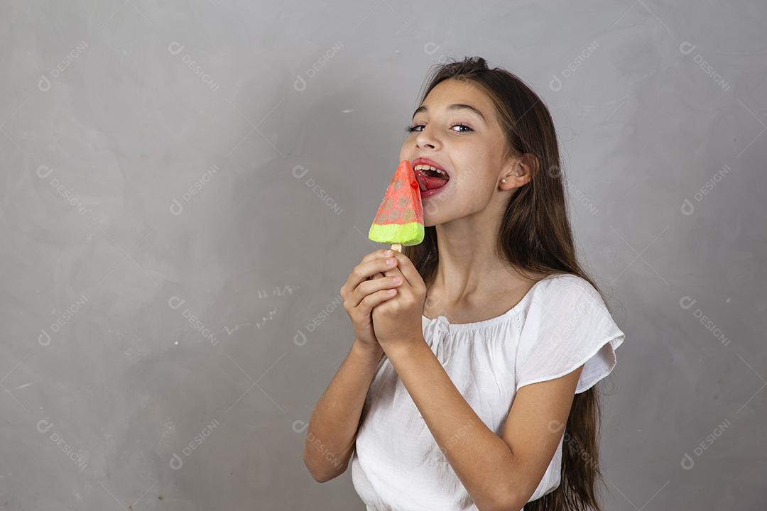 Adorável menina com delicioso picolé de sorvete no fundo cinza
