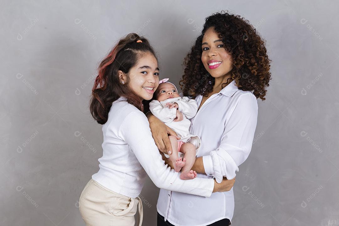 Linda jovem mãe afro com suas filhas em fundo cinza. Mãe, filha e bebê