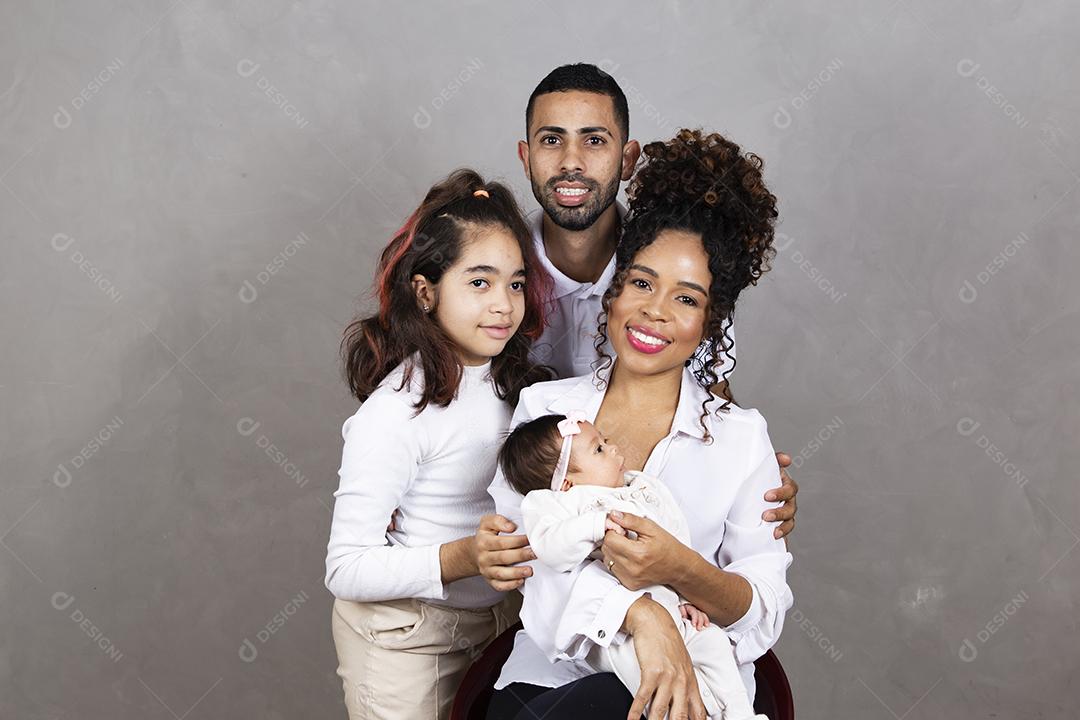 Lindos pais jovens com suas filhas em fundo cinza. Irmã mais velha, bebê recém-nascido, mãe e pai felizes