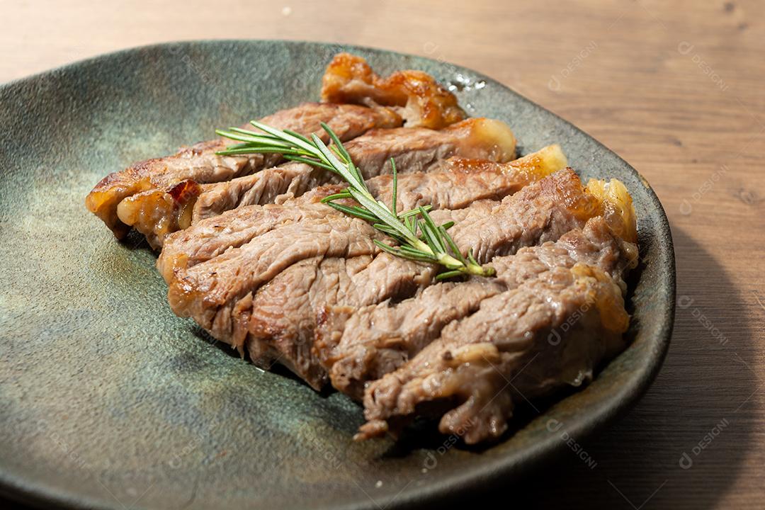 delicioso rosbife, em um prato preto e superfície de madeira, com um raminho de tomilho por cima
