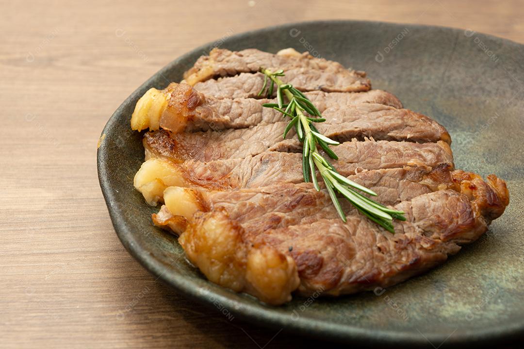 delicioso rosbife, em um prato preto e superfície de madeira, com um raminho de tomilho por cima