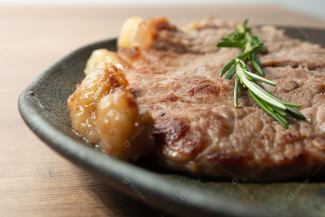 delicioso rosbife, em um prato preto e superfície de madeira, com um raminho de tomilho por cima