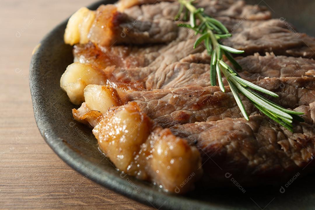 Tiro de delicioso rosbife, em uma placa preta e superfície de madeira, com um raminho de tomilho por cima