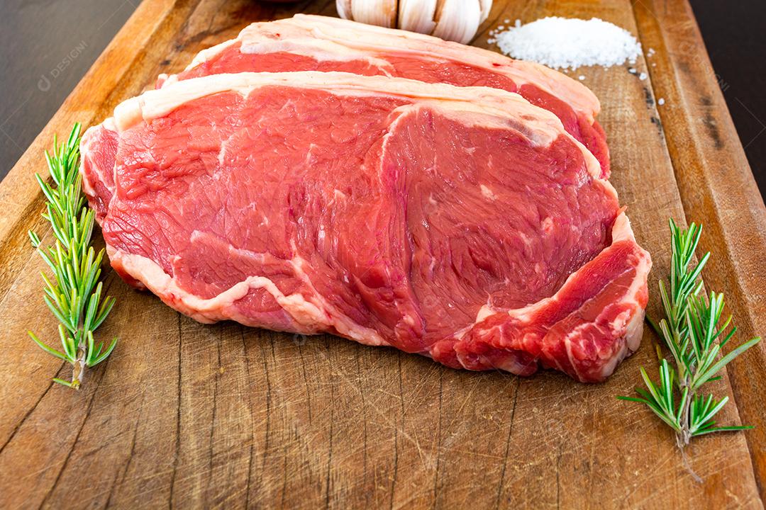 carne vermelha crua, bife do lombo com gordura em uma tábua de corte junto com tomilho, alho, cebola e sal. temperos naturais prontos para o churrasco no quintal da família