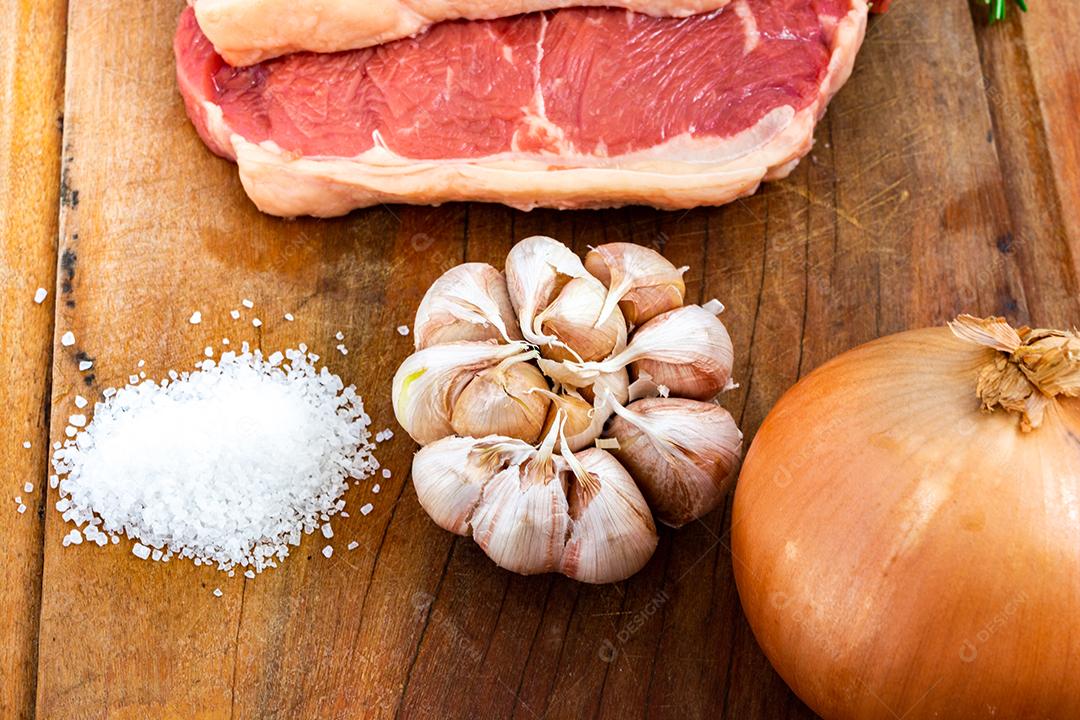 tong pegando carne vermelha crua, bife do lombo com gordura em uma tábua de corte junto com tomilho, alho, cebola e sal