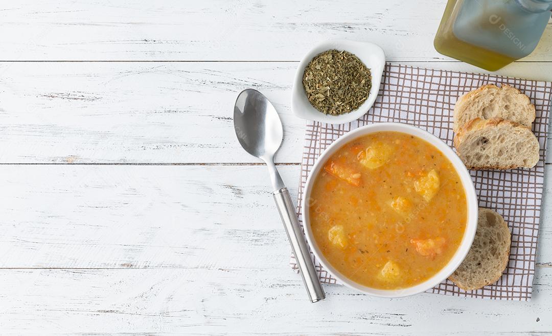 Sopa de legumes em uma tigela com temperos e fatias de pão sobre mesa de madeira .