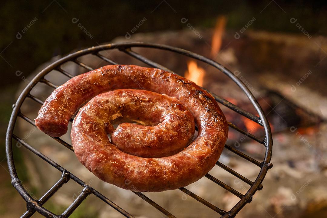 Salsicha caseira brasileira assando na grelha sobre brasas.
