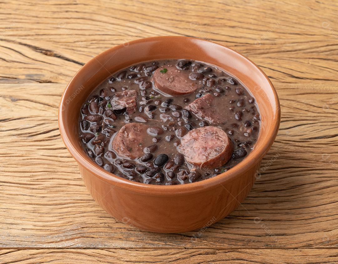 Feijoada tradicional brasileira em uma tigela sobre a mesa de madeira.