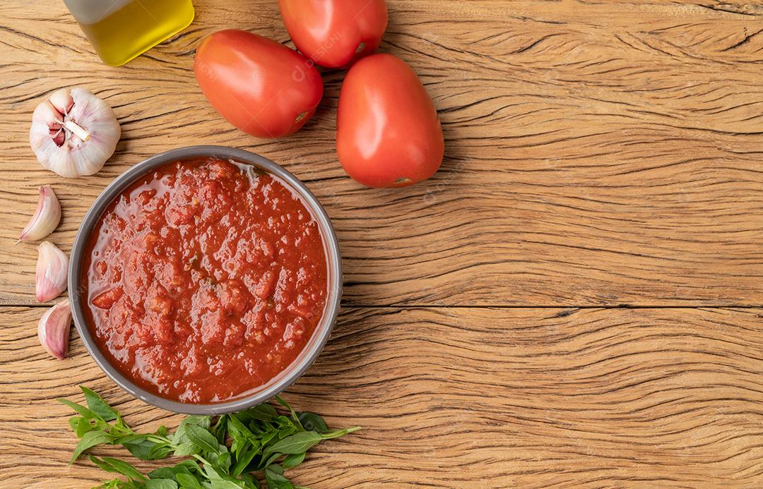 Molho de tomate, tomate, alho, azeite e ervas sobre a mesa de madeira