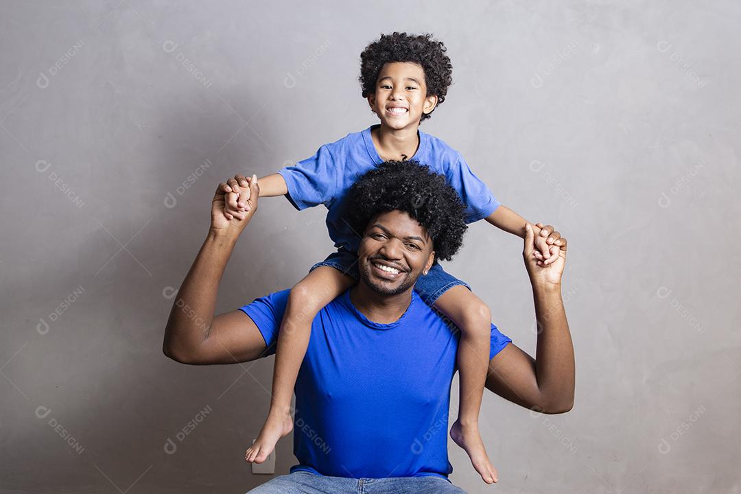 son sitting on father's shoulder on gray background. Happy afro father and son