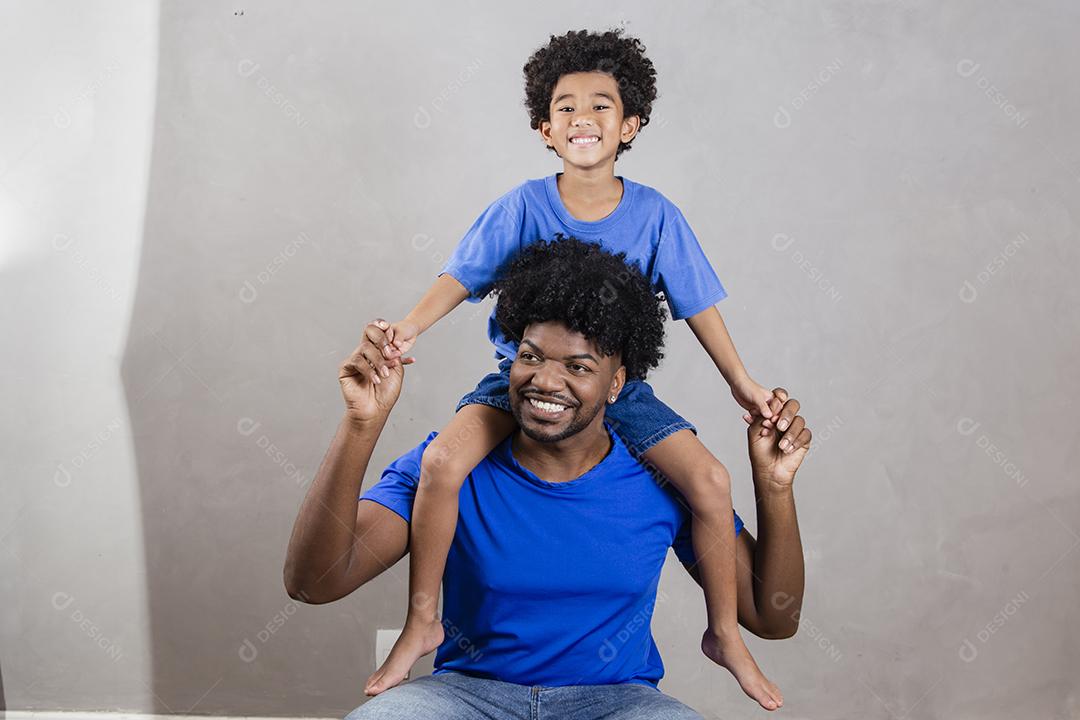 filho sentado no ombro do pai em fundo cinza. Feliz afro pai e filho