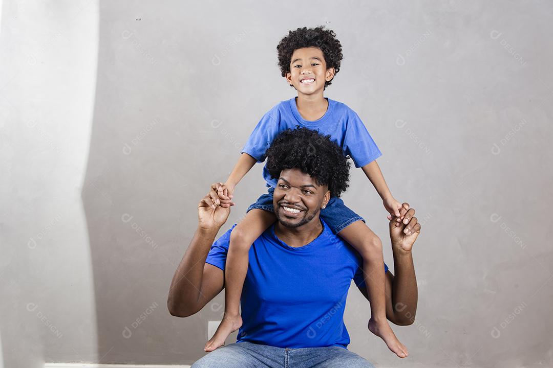 filho sentado no ombro do pai em fundo cinza. Feliz afro pai e filho