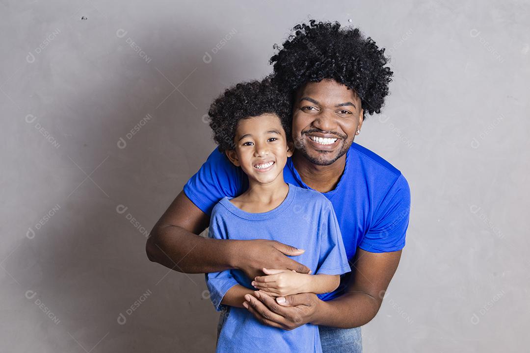 filho sentado no ombro do pai em fundo cinza. Feliz afro pai e filho
