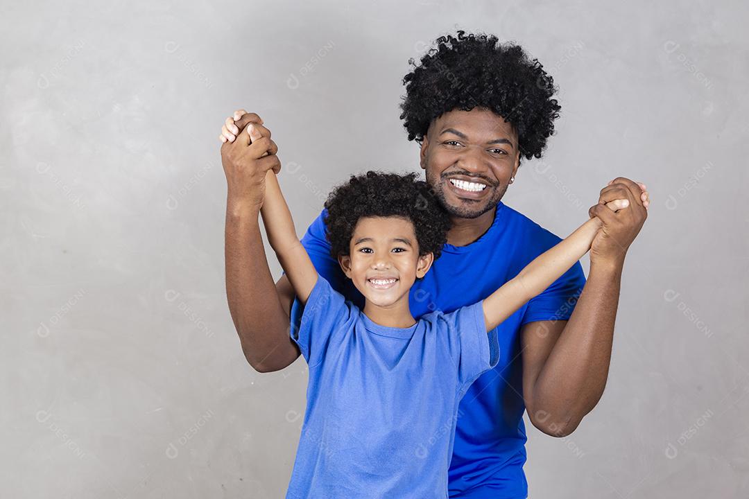 filho sentado no ombro do pai em fundo cinza. Feliz afro pai e filho