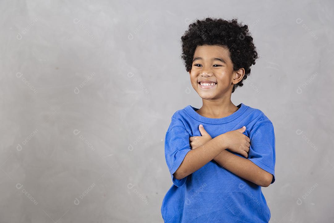 adorável menino afro com braços cruzados sorrindo em fundo cinza