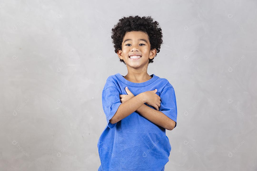 adorável menino afro com braços cruzados sorrindo em fundo cinza