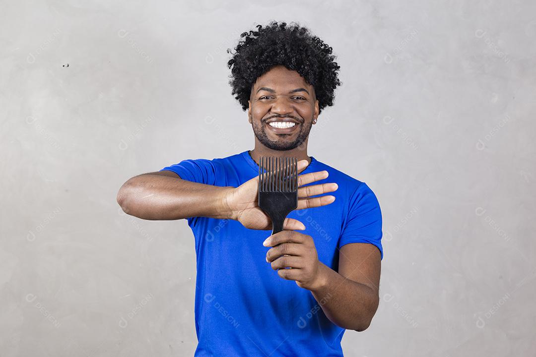 Jovem latino penteando o cabelo. Garfo para pentear cabelos cacheados. Fundo cinza.