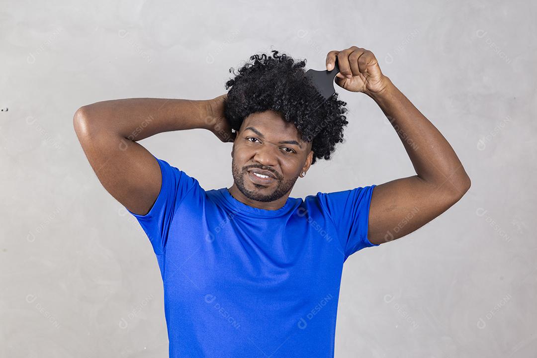 Jovem latino penteando o cabelo. Garfo para pentear cabelos cacheados. Fundo cinza.