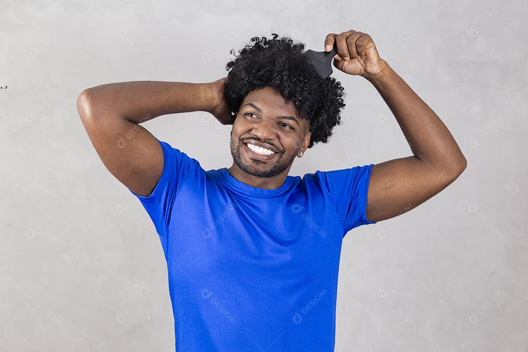 Jovem latino penteando o cabelo. Garfo para pentear cabelos cacheados. Fundo cinza.