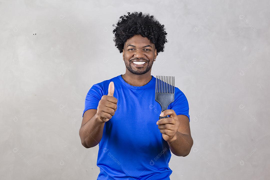 Jovem latino penteando o cabelo. Garfo para pentear cabelos cacheados. Fundo cinza.