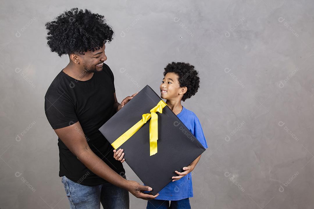 afro pai e filho em fundo neutro com presente