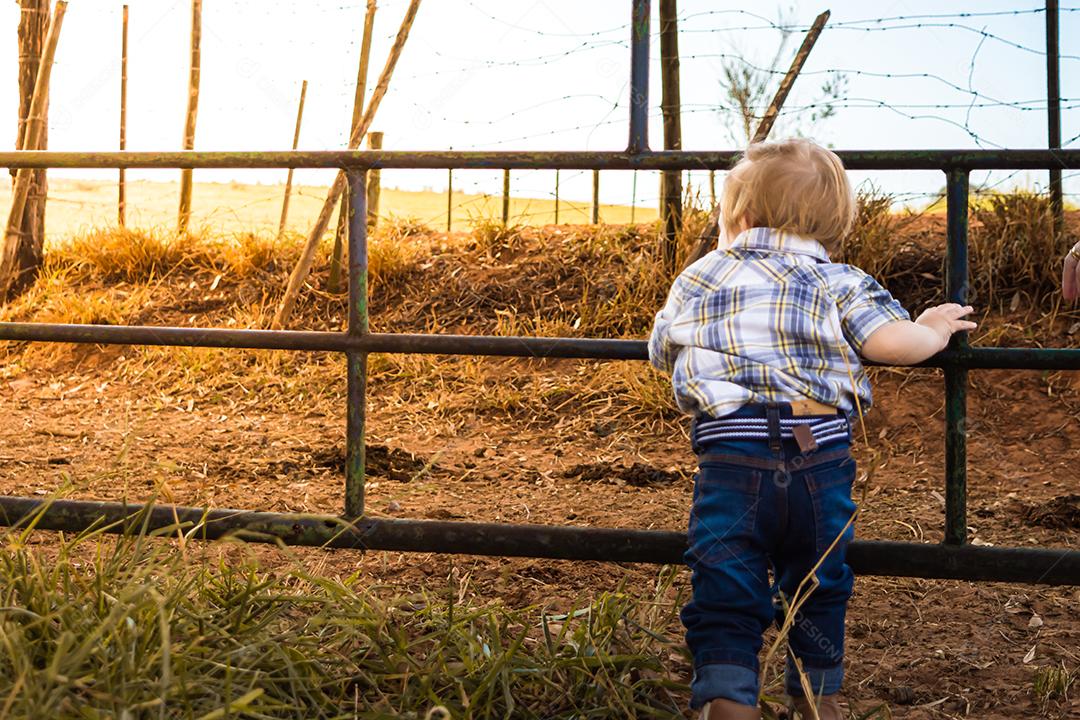menino vestido de cowboy ou peão olhando para longe em um portão de sitio