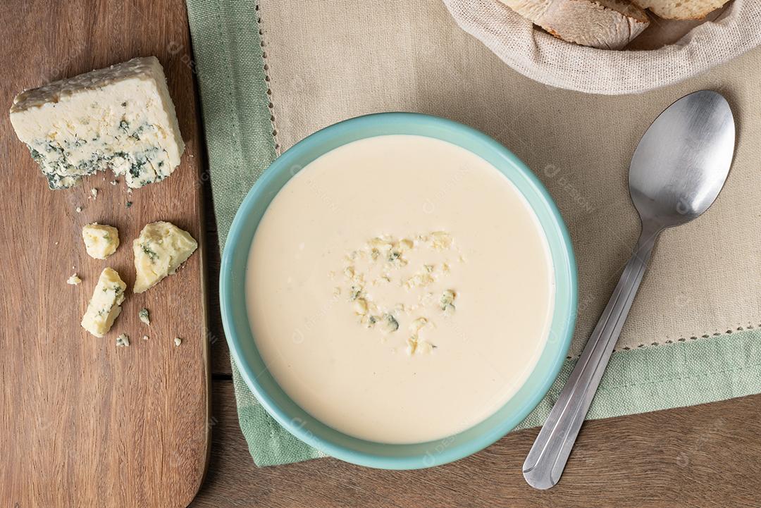 Sopa de queijo em uma tigela com fatias de pão sobre a mesa de madeira.