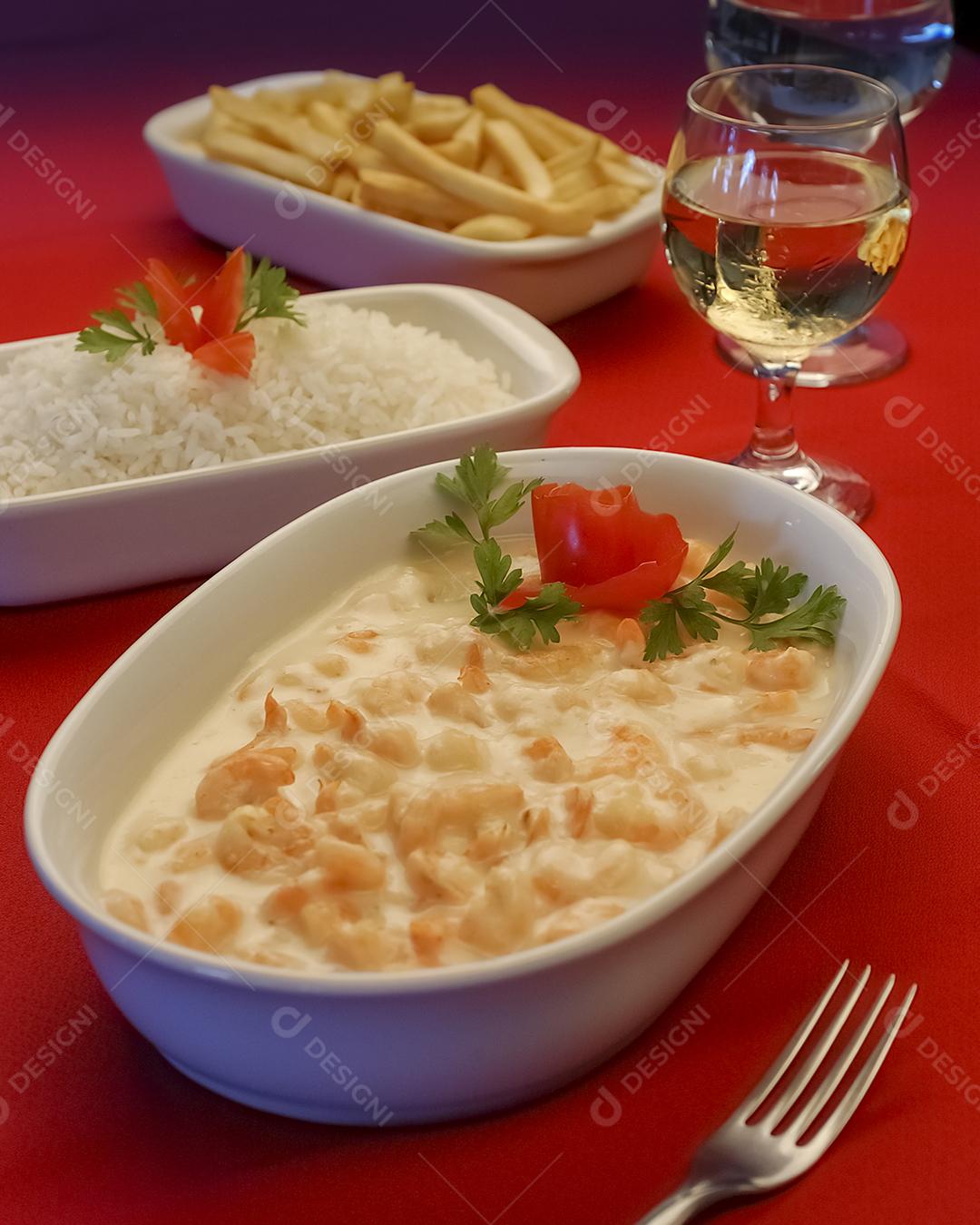 Camarão em molho de queijo branco em tigela branca na toalha de mesa vermelha.