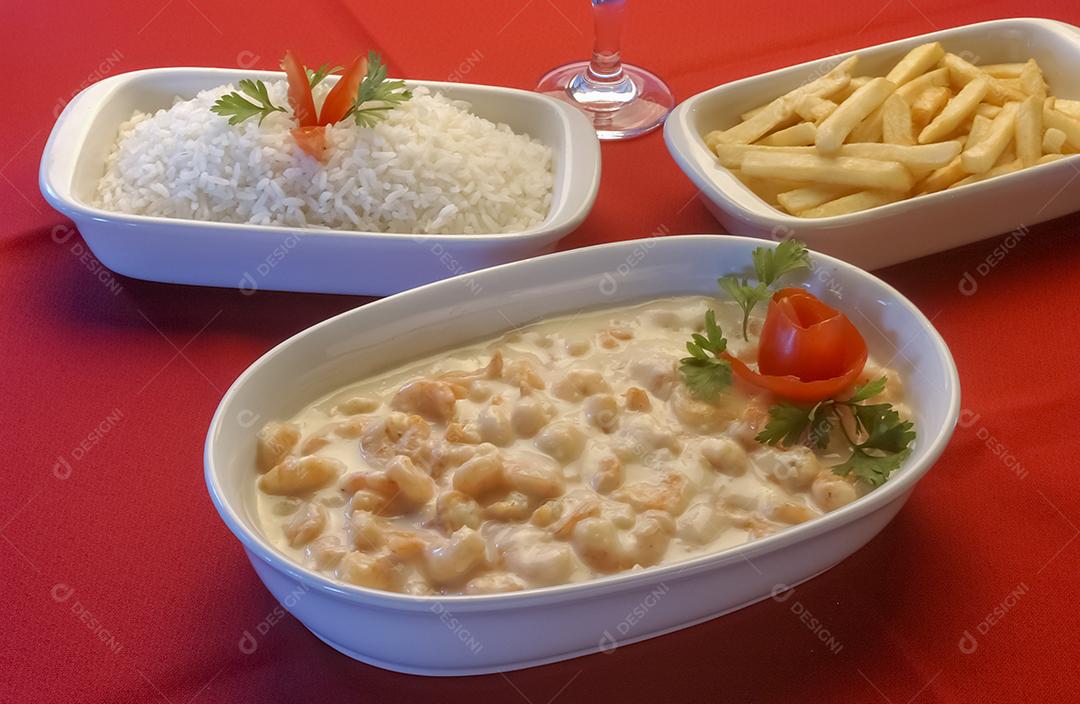 Camarão em molho de queijo branco em tigela branca na toalha de mesa vermelha.