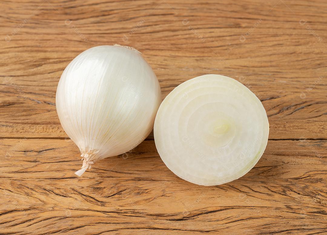 Cebola branca com metade sobre a mesa de madeira.