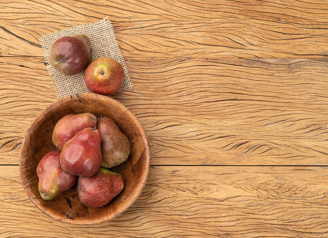 Peras vermelhas em uma tigela sobre mesa de madeira com espaço de cópia.