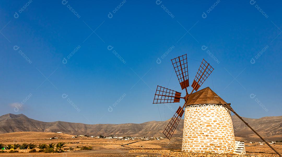 Moinho de vento velho na ilha de Fuerteventura com as montanhas do deserto ao fundo