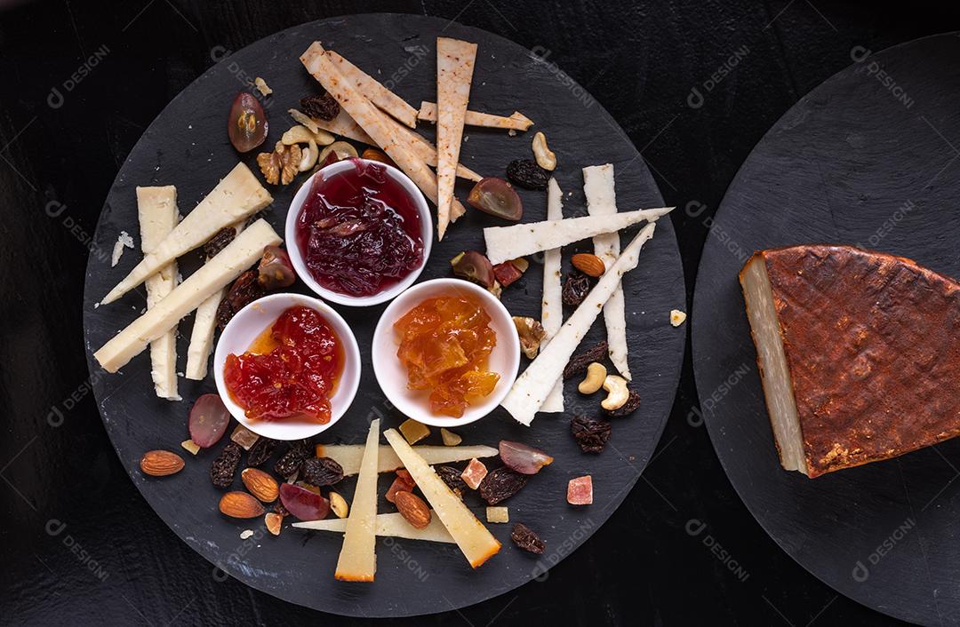 Tábua de queijos com nozes e marmeladas em um fundo de ardósia preta