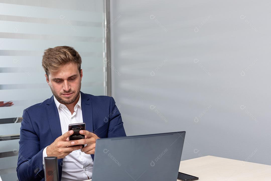 Homem de negócios jovem no escritório enviando mensagens de texto na frente do laptop
